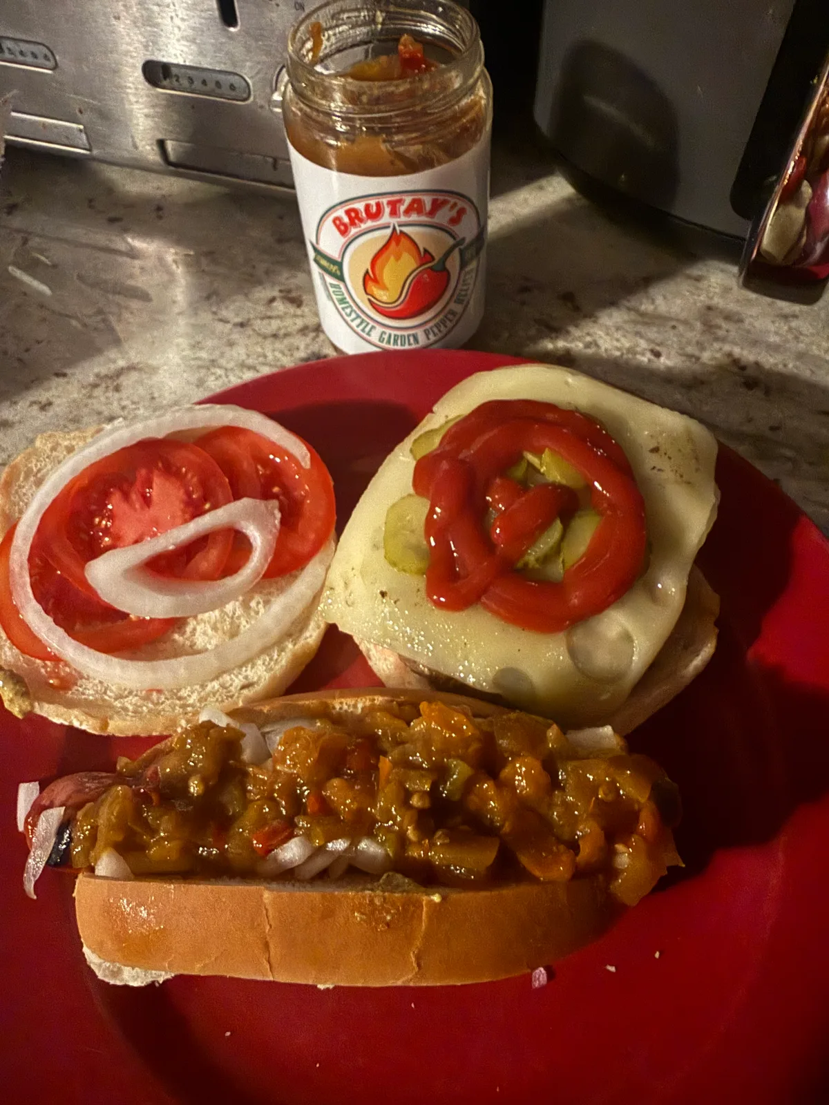 Open hot dog topped with Brutay's Homestyle Garden Pepper Relish beside a sliced burger bun with tomato and onion