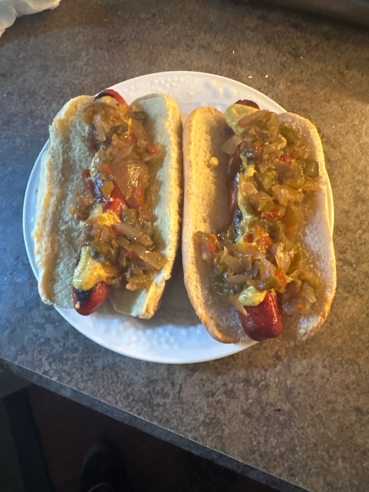 Two grilled hot dogs loaded with Brutay's pepper relish and mustard on a white plate