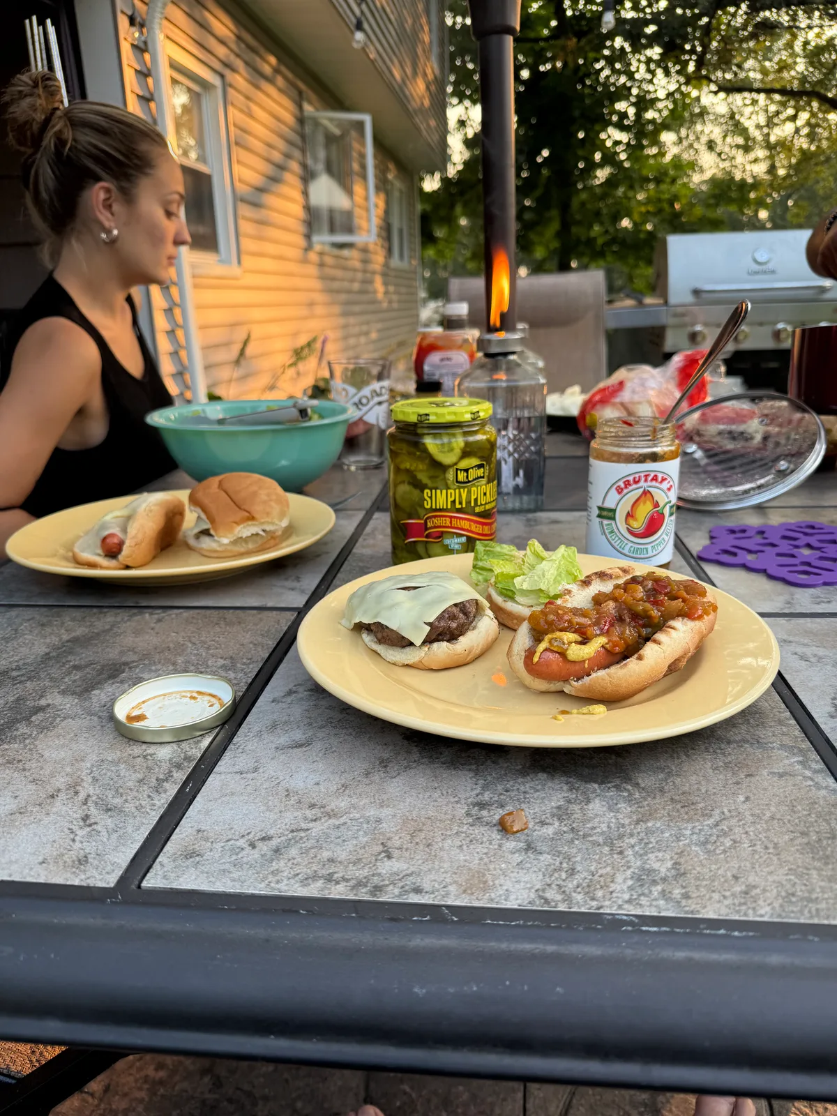 Backyard dinner table with hot dogs, a cheeseburger, and a jar of Brutay's Homestyle Garden Pepper Relish